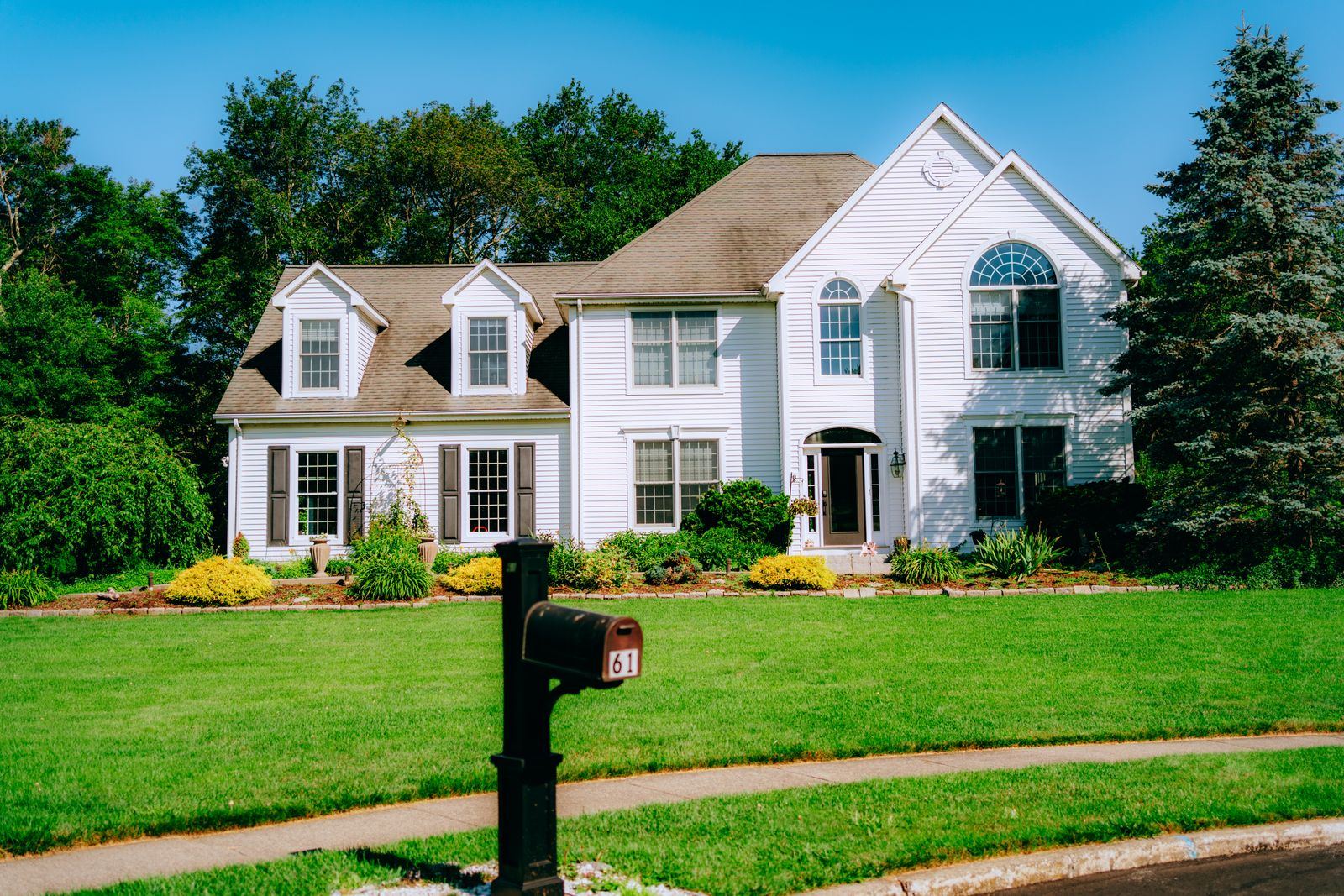 Two-story colonial home with a green front lawn and landscaped beds